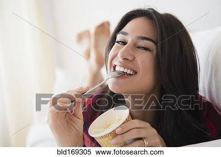 Stock Photography - Close up of woman eating ice cream on sofa. Fotosearch