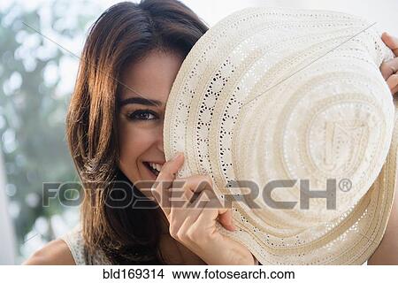 Picture - Close up of woman hiding behind sun hat. Fotosearch