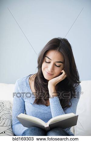 Stock Image - Close up of woman reading book on sofa. Fotosearch