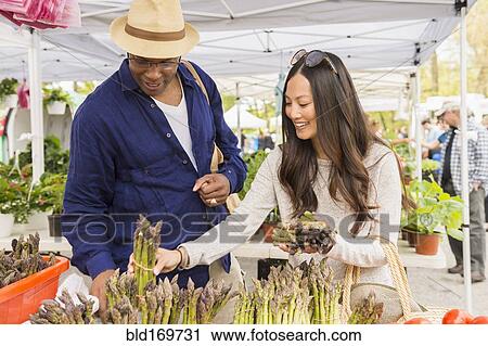 Stock Image - Couple shopping for asparagus in farmers market. Fotosearch