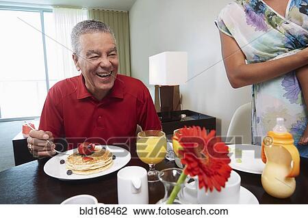 Stock Image - Father and daughter eating pancakes at table. Fotosearch
