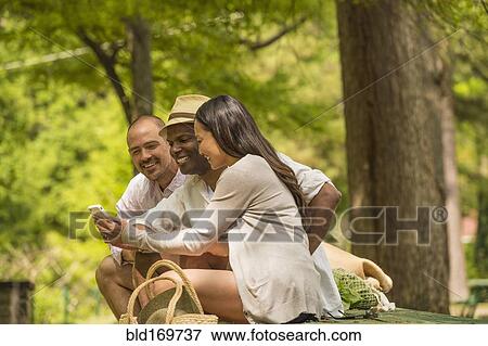 Stock Photo - Friends using cell phone on picnic table. Fotosearch