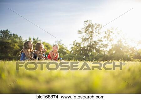 Picture - Girls blowing bubbles in grass field. Fotosearch