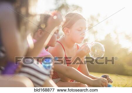 Stock Photo - Girls blowing bubbles in grass field. Fotosearch
