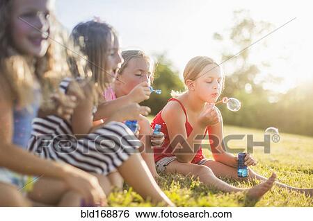 Girls blowing bubbles in grass field View Large Photo Image Stock Photograph - Girls blowing bubbles in grass field. Fotosearch