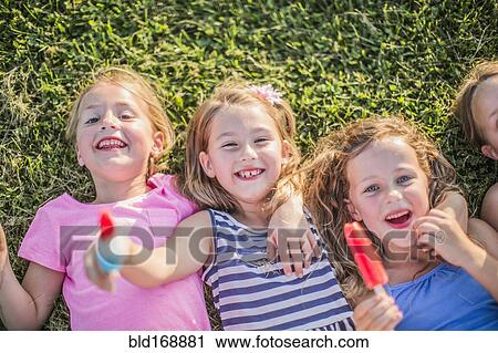 Stock Image - Girls eating flavored ice in grass. Fotosearch