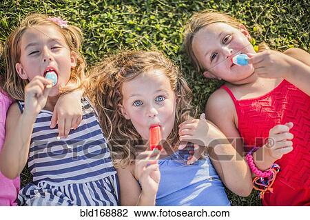 Stock Image - Girls eating flavored ice in grass. Fotosearch