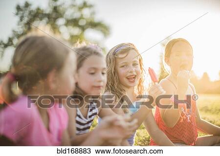 Stock Image - Girls eating flavored ice in sunny field. Fotosearch