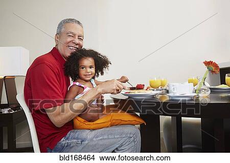 Picture - Grandfather and granddaughter eating breakfast at table. Fotosearch