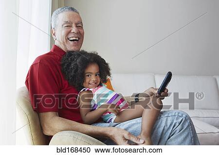 Stock Image - Grandfather and granddaughter sitting on sofa. Fotosearch