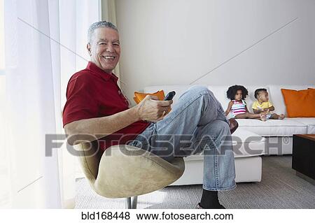 Stock Photo - Grandfather relaxing with grandchildren in living room. Fotosearch