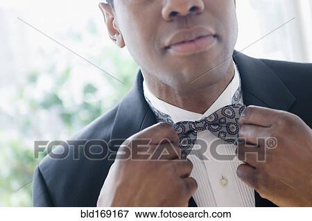 Stock Photo - Groom in tuxedo adjusting bow tie. Fotosearch