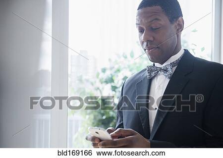 Stock Photograph - Groom in tuxedo using cell phone. Fotosearch