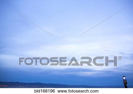 Stock Photograph - Hand holding cell phone under twilight sky. Fotosearch
