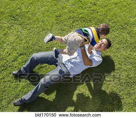 Stock Image - High angle view of Hispanic father and son playing on lawn. Fotosearch
