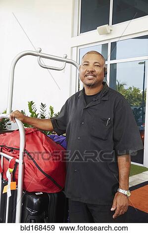 Stock Photo - Hispanic bellboy holding luggage at hotel. Fotosearch