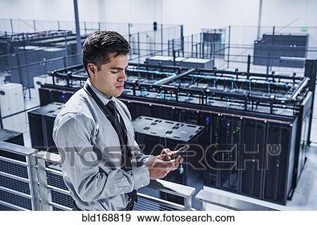 Stock Photo - Hispanic businessman using cell phone on balcony over server room. Fotosearch