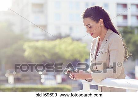 Stock Photo - Hispanic businesswoman using cell phone outdoors. Fotosearch