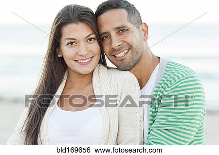Stock Photograph - Hispanic couple hugging on beach. Fotosearch