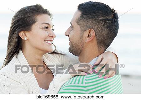 Stock Photography - Hispanic couple hugging on beach. Fotosearch