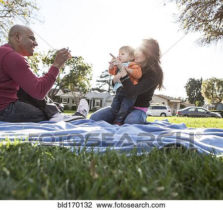 Stock Image - Hispanic family on blanket in park. Fotosearch