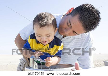 Stock Image - Hispanic father and son playing with water fountain. Fotosearch