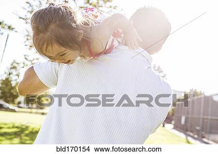 Picture - Hispanic father carrying daughter on shoulders. Fotosearch