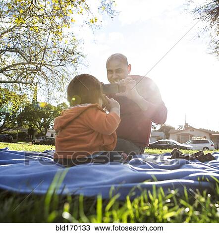 Hispanic father photographing son on blanket in park View Large Photo Image Stock Image - Hispanic father photographing son on blanket in park. Fotosearch