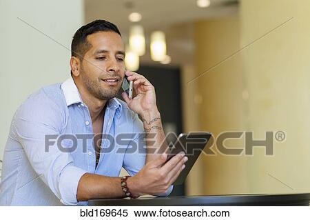 Stock Photography - Hispanic man using digital tablet and cell phone. Fotosearch