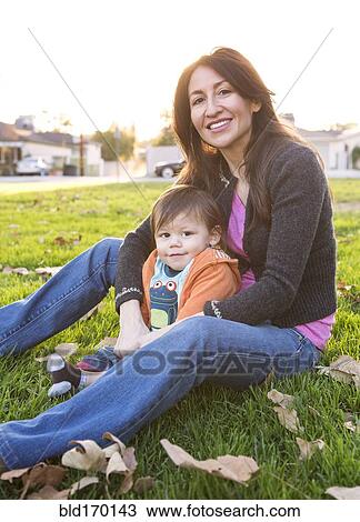 Stock Image - Hispanic mother sitting with son in park. Fotosearch