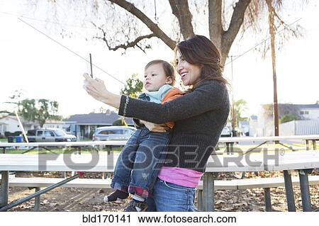 Stock Image - Hispanic mother taking selfie with son in park. Fotosearch