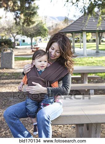 Hispanic mother wearing son in carrier in park View Large Photo Image Picture - Hispanic mother wearing son in carrier in park. Fotosearch