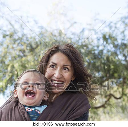 Stock Photograph - Hispanic mother wearing son in carrier outdoors. Fotosearch