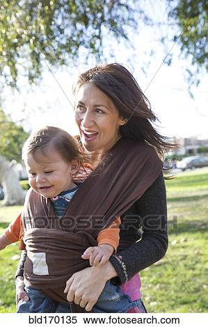 Stock Photography - Hispanic mother wearing son in carrier in park. Fotosearch