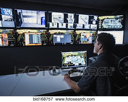 Stock Photo - Hispanic security guard watching monitors in control room. Fotosearch