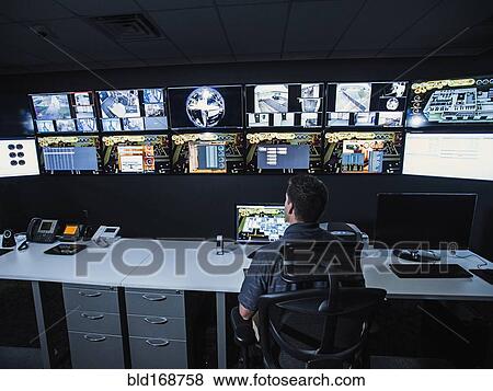 Stock Photo - Hispanic security guard watching monitors in control room. Fotosearch