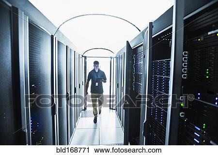 Stock Image - Hispanic technician carrying digital tablet in server room. Fotosearch