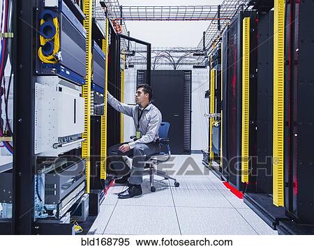 Stock Photography - Hispanic technician examining computer in server room. Fotosearch