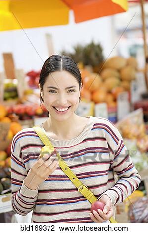 Stock Image - Hispanic woman eating fruit at farmers market. Fotosearch
