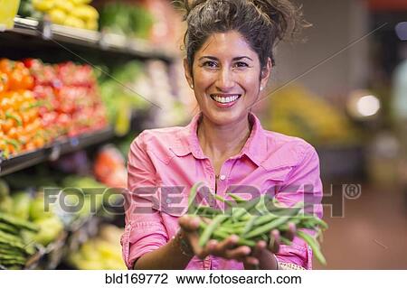 Stock Image - Hispanic woman holding vegetables at grocery store. Fotosearch