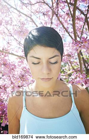 Picture - Hispanic woman standing under flowering tree. Fotosearch