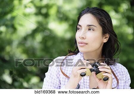 Stock Photo - Hispanic woman using binoculars outdoors. Fotosearch