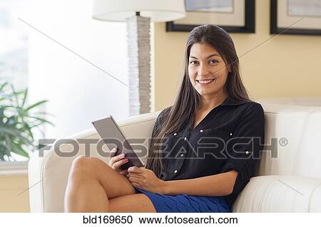 Stock Image - Hispanic woman using digital tablet in armchair. Fotosearch