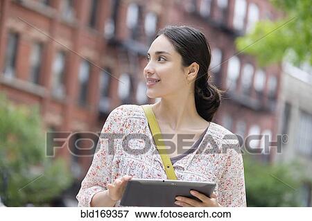 Stock Photo - Hispanic woman using digital tablet in city. Fotosearch