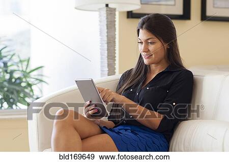 Stock Photo - Hispanic woman using digital tablet in armchair. Fotosearch