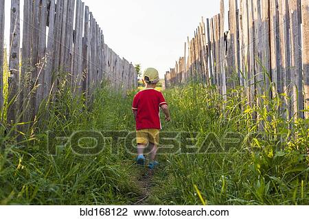Stock Image - Mari boy walking in grass between fences. Fotosearch