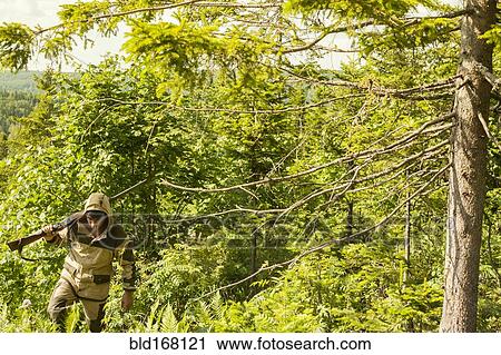 Stock Image - Mari man with gun climbing forest hill. Fotosearch