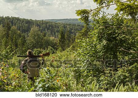 Stock Image - Mari man with gun overlooking rural landscape. Fotosearch