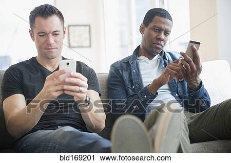 Stock Image - Men using cell phones on sofa. Fotosearch