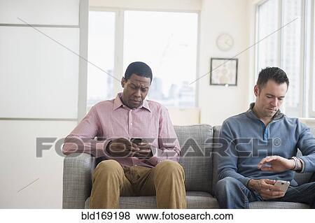 Stock Photo - Men with cell phones waiting on sofa. Fotosearch